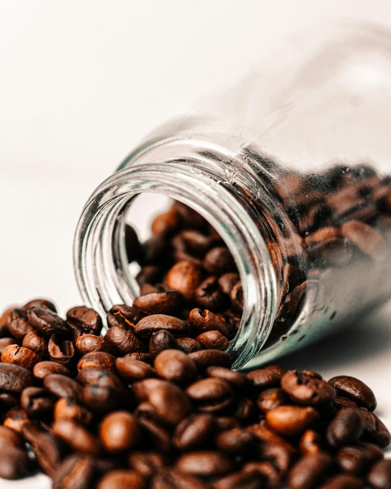 Close-up of aromatic coffee beans spilling from a glass jar showcasing rich brown tones.
